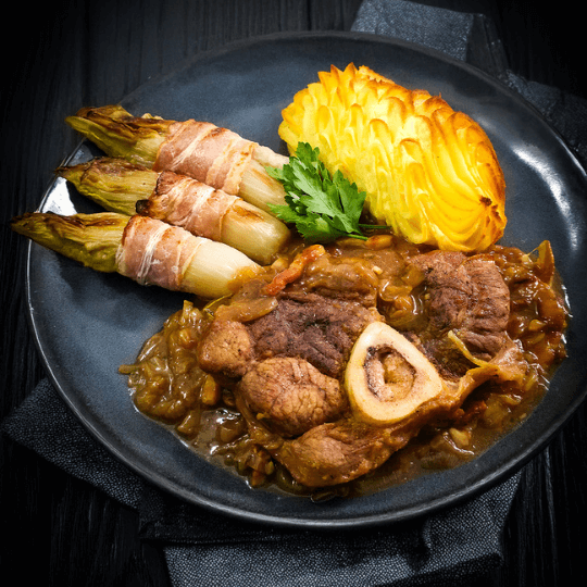 Kalfsschenkel traag gegaard in uiensaus van Gouden Carolus Classic met witloof en pommes dauphinois